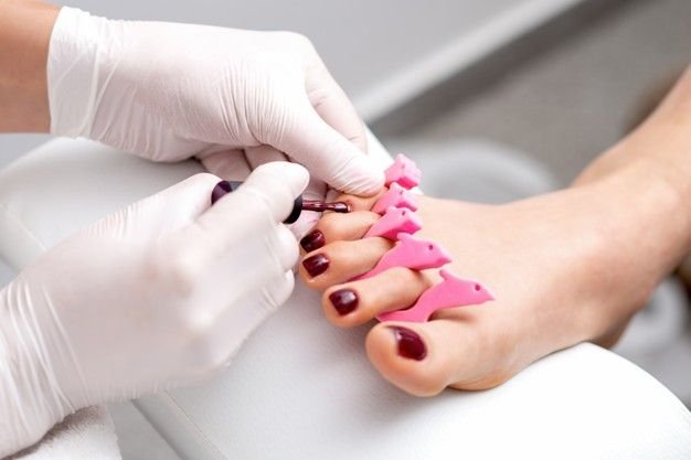 Premium Photo _ Manicure master is painting on female toenails with maroon nail polish by brush wearing white gloves